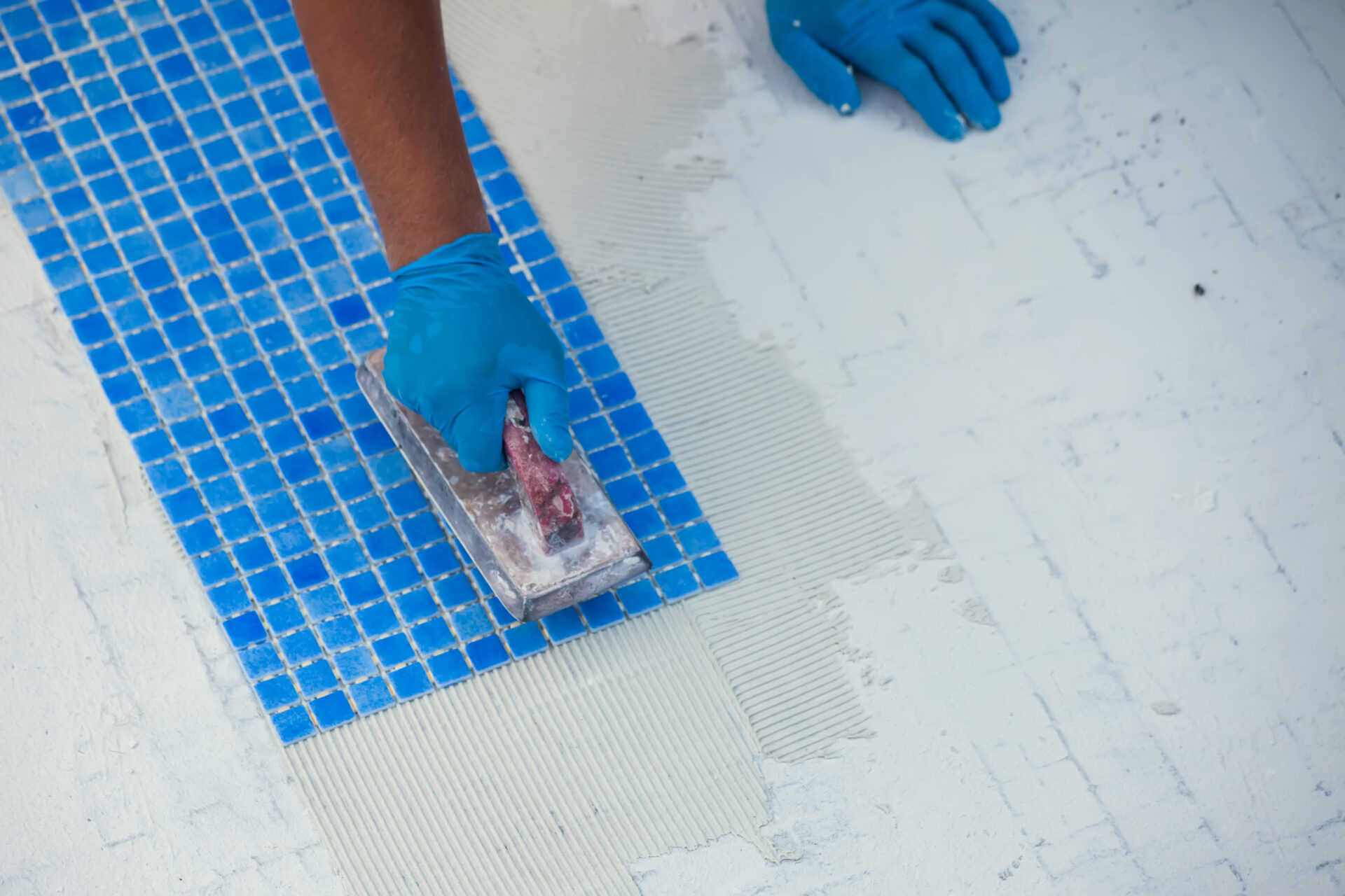 Worker laying tile in the pool. Pool repairing work.