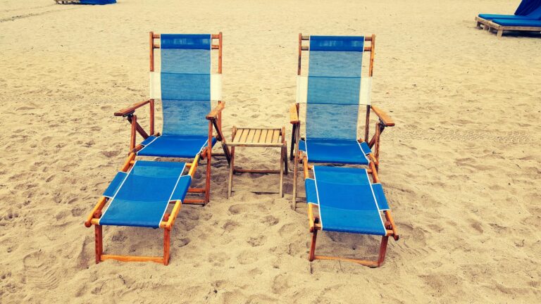 Relaxing beach scene with two blue sun loungers on sandy shore, perfect for tropical vacations.